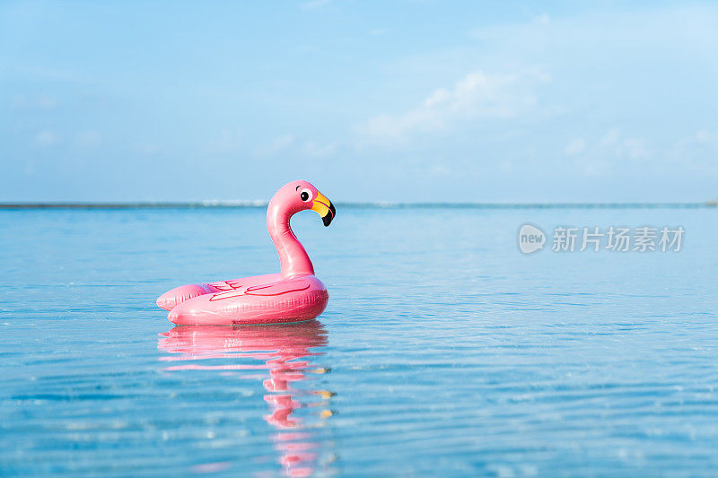 充气粉红色火烈鸟漂浮在透明的绿松石海。蓝色的天空，很少有云的背景。