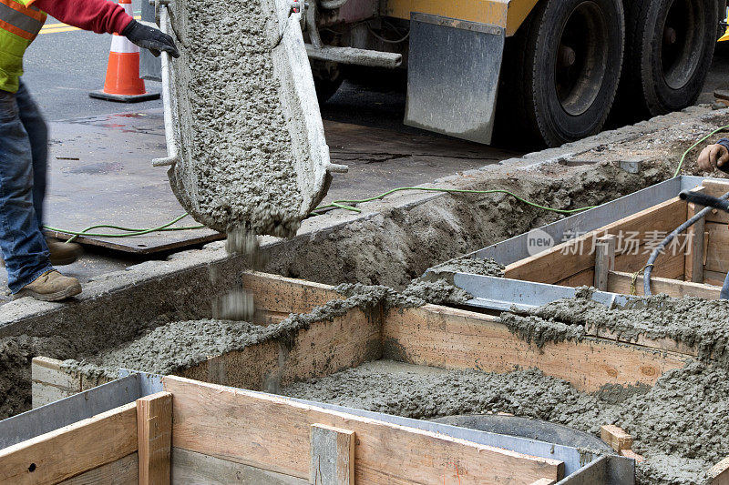 工人从城市街道的水泥卡车上引导水泥进入框架
