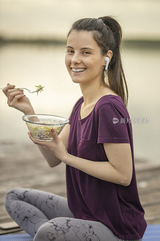 听着音乐，吃着沙拉，坐在湖边码头上的女人