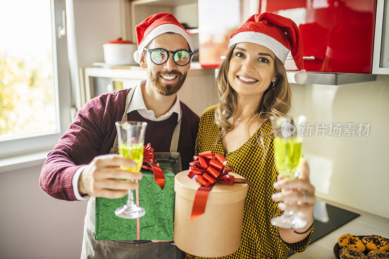 浪漫的情侣在家里交换圣诞礼物。丈夫和妻子在厨房里交换圣诞礼物，喝香槟