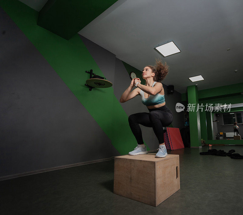一个年轻健康的女人在体育课上跳在木箱上。功能训练,锻炼。