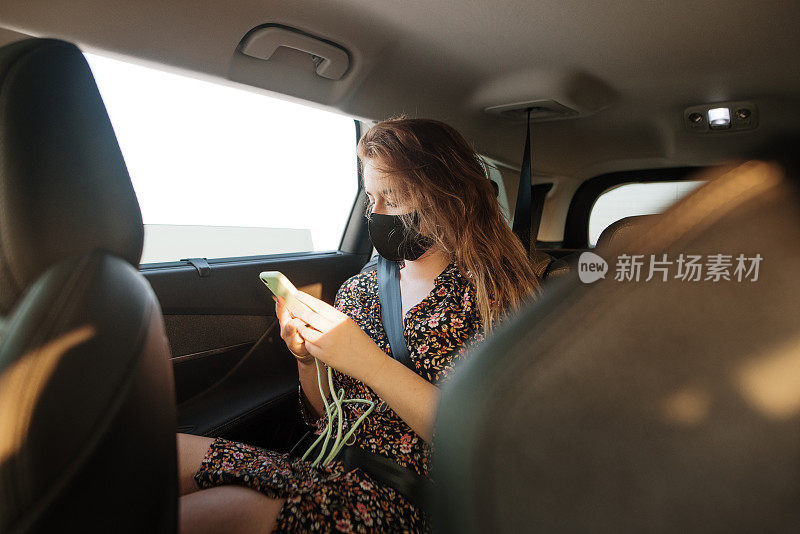 年轻女子戴着口罩在汽车后座上打电话