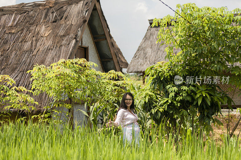 亚洲孕妇在稻田和她传统的房子里