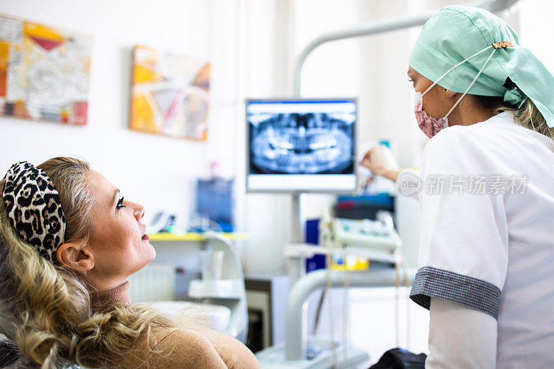 一位女牙医一边和病人说话，一边指着数码牙科x光片