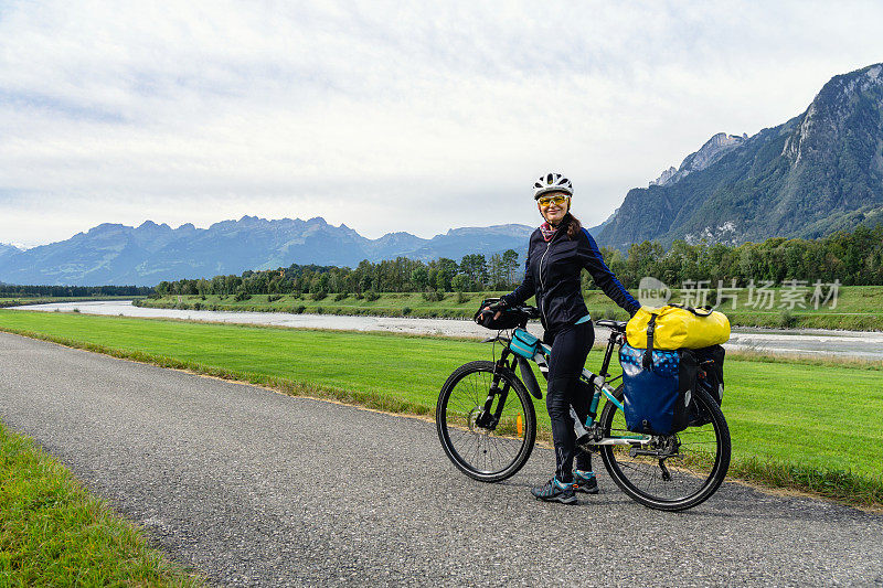 骑自行车的女人沿着河边和山上的自行车道骑车旅行。阿尔卑斯山的背景。欧洲,瑞士。