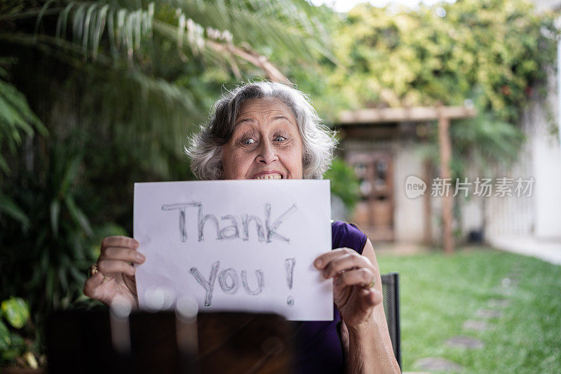 妇女在家视频电话拿着写有“谢谢”的纸在家