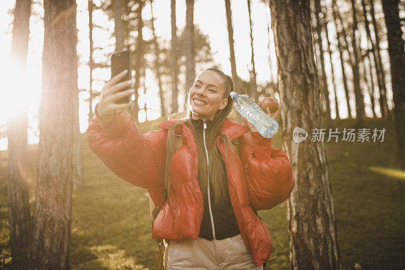 女人徒步旅行者用她的智能手机自拍和徒步在日出的山峰