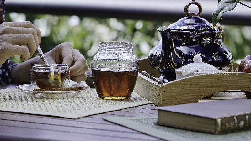 近距离观察年轻女子的手倒蜂蜜天然甜味剂热茶杯在一张桌子上的户外露台