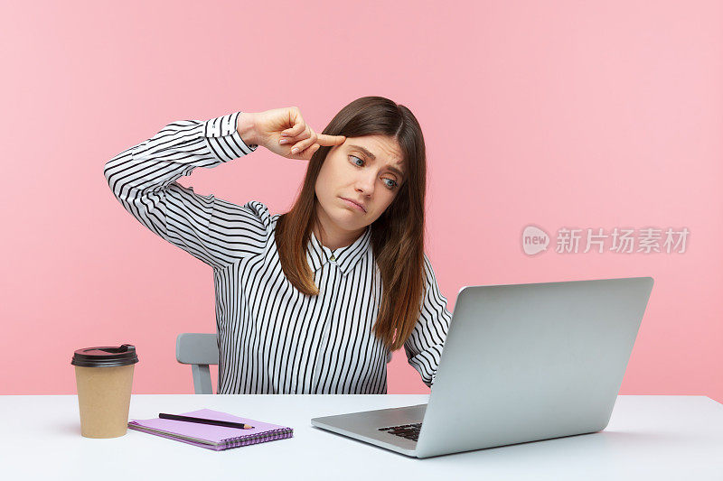沮丧不快乐的女办公室工作人员在条纹衬衫坐在工作场所显示愚蠢的手势对笔记本电脑显示视频通话