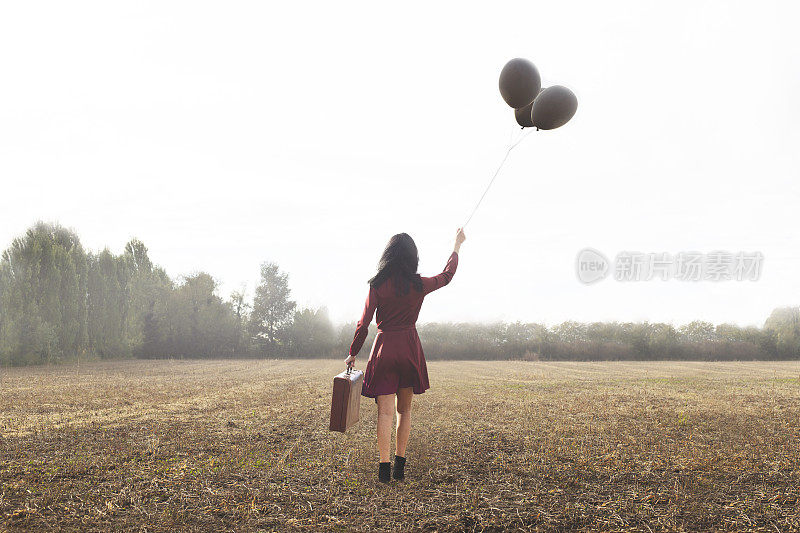 年轻的旅行者带着她的旅行箱和气球向未知的地方走去
