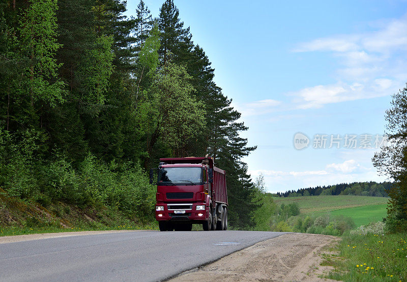 自卸卡车沿着公路行驶，从采石场运送沙子。运输散装货物的现代重型自卸车。卡车在路