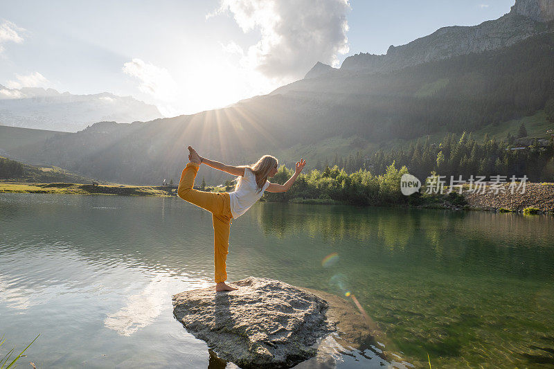 一名年轻女子在湖上的岩石上练习瑜伽