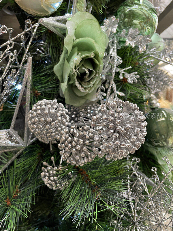 图像的人造，绿色玫瑰花头装饰挂在人造圣诞树的树枝，银色的常春藤浆果和叶子，绿色云杉针，模糊的白色精灵灯的背景