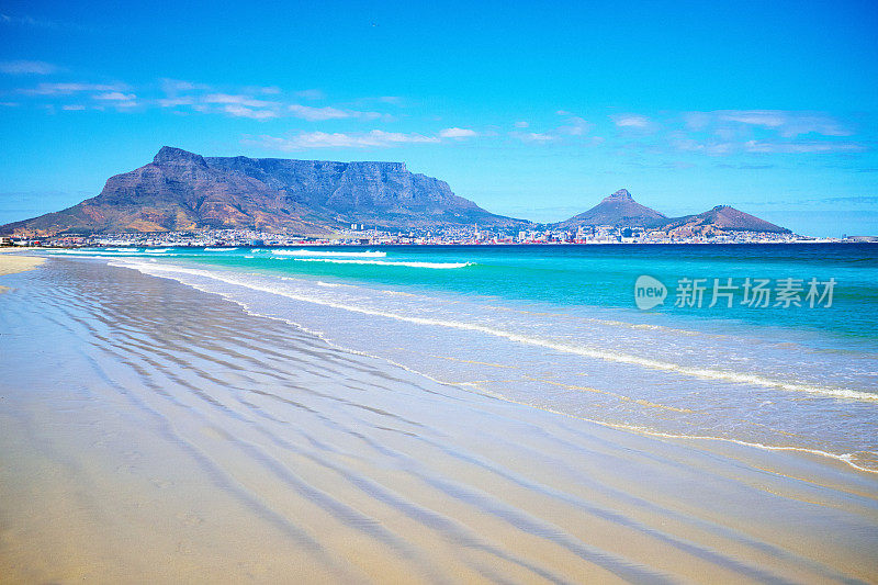 在一个明媚的夏日，从一个荒凉的日落海滩上，可以看到南非桌山和开普敦的经典景色