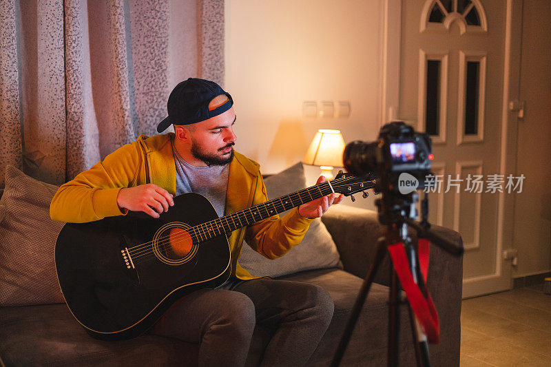 留着大胡子的年轻音乐老师，一边在家里弹吉他，一边用单反相机为YouTube录制教程