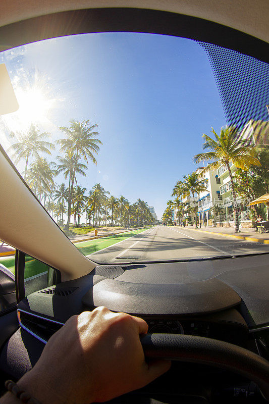 一个年轻的运动男子的视角拍摄在迈阿密海滩艺术装饰区，迈阿密，南佛罗里达，美国，在天堂蓝色的海洋景观前驾驶一辆汽车