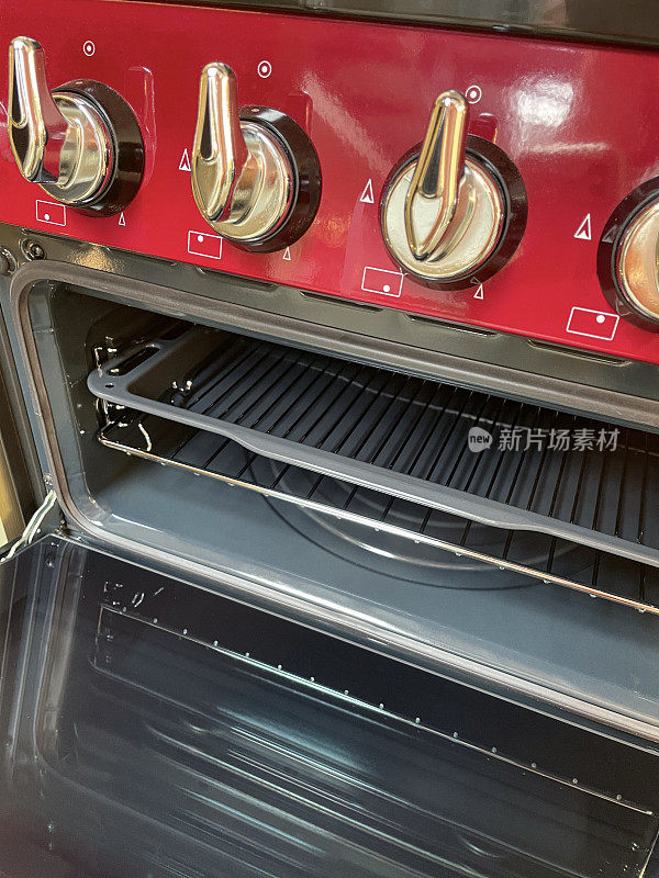 红色的特写图像，煤气灶烤箱，打开的烤箱门，货架架，旋钮控制面板，前景聚焦