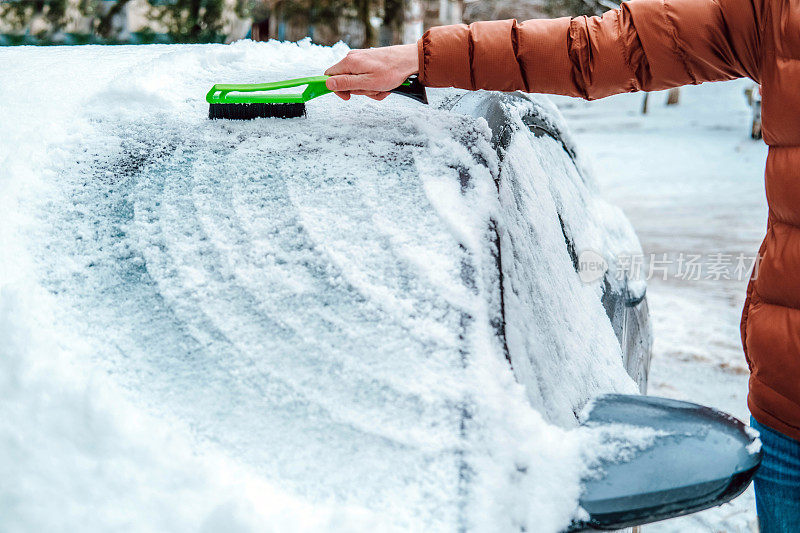 一名男子手里拿着一把刷子，正在擦车窗上的雪。交通的概念，冬天，天气，人和车辆。