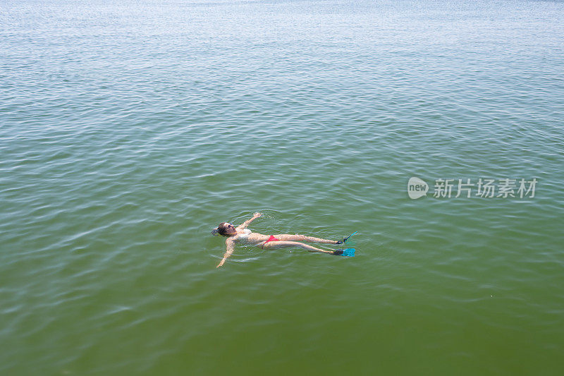 年轻女子仰面在海里游泳。