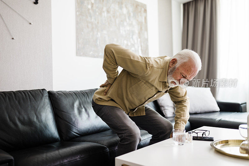 老男人觉得不舒服，背痛，坐在家里客厅的沙发上按摩酸痛的肌肉。长者与健康问题的概念