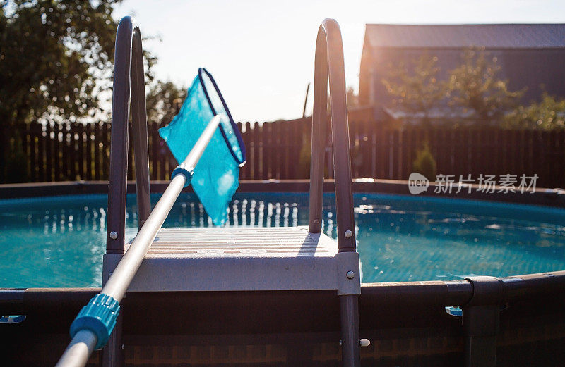 用带网眼的金属框架清理游泳池的污垢。操作期间的池清洁剂。太阳能旗帜。暑假的概念。抽象模糊和散焦背景。