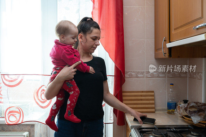 母亲把女儿抱在怀里，从厨房的工作台上拿了一部智能手机。
