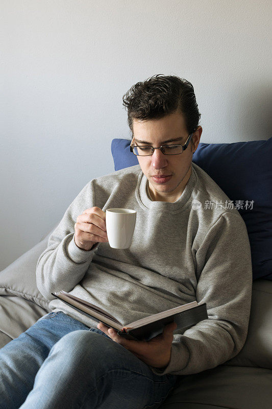 年轻人坐在床上一边喝咖啡一边看书