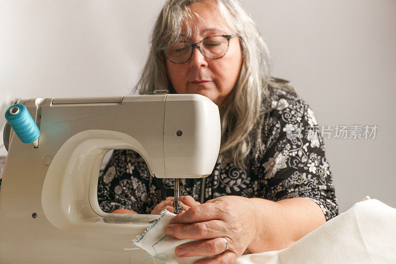 白发苍苍的老妇人正在缝纫机上缝布料