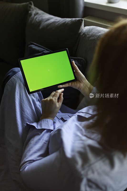 一个女人坐在家里的沙发上用平板电脑