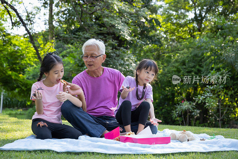 幸福美满的家庭。爷爷和孙女轮流喂对方甜甜圈，在公园里玩得很开心。