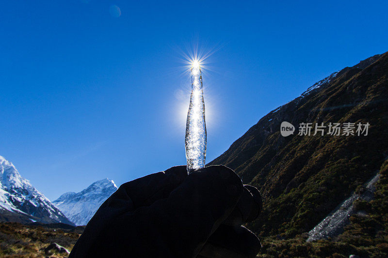 在阳光直射下，由戴手套的人握住带有太阳耀斑的冰冻水冰柱