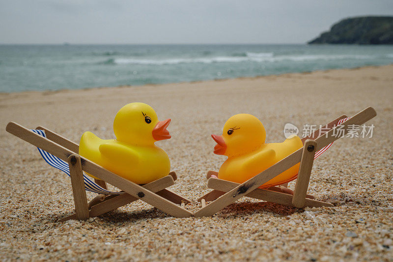 概念性的，一对在海滩度假的夫妇，两只橡皮鸭坐在康沃尔郡佩顿温德海滩上的迷你躺椅上。