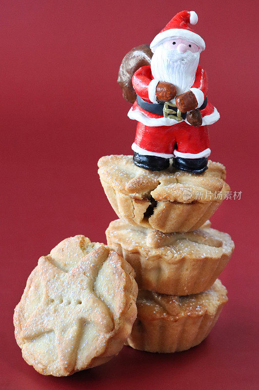 单个肉馅饼的形象靠在三个肉馅饼的堆栈，圣诞老人雕像站在塔顶，红色背景，重点在前景，圣诞食品的概念