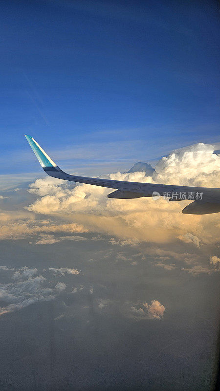 透过窗户看飞机在飞行与翅膀和蓝天云在日落。