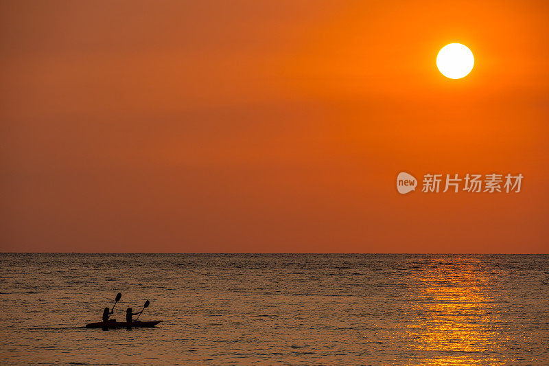 两人划着皮艇，天际线的景观背景夕阳在傍晚的天空与彩色的云和美丽的云图案在柔和的黄昏的光在海上。
