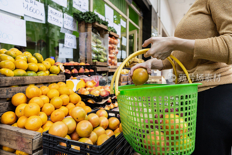 在街边的杂货店里，一位顾客举着购物篮挑选水果和蔬菜的特写