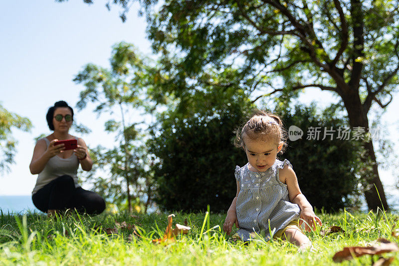 妈妈在公园用智能手机拍摄她的宝贝女儿