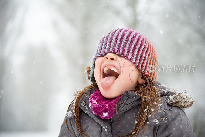 小女孩在雪中玩耍，她试图用她的嘴去接雪花