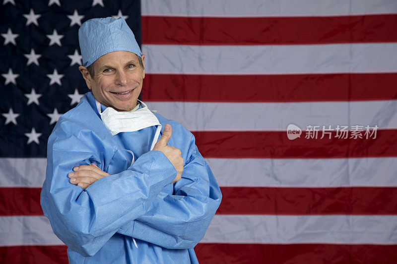外科医生站在美国国旗前，微笑着竖起大拇指，看着镜头