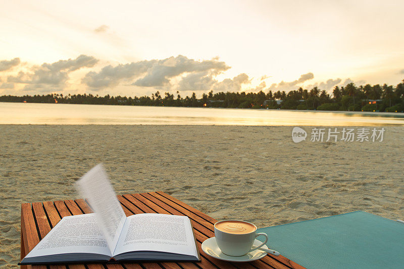 在日出时分打开热带海边沙滩桌上的书和咖啡杯