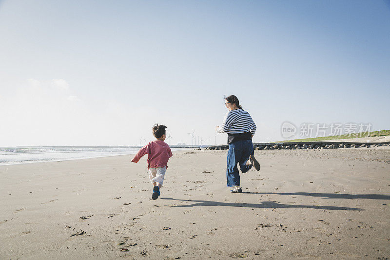 母亲和儿子在海滩上跑步，靠近风力发电场