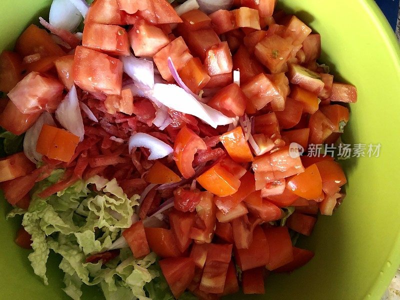 这是一碗沙拉，由切碎的番茄、切碎的莴苣叶和切碎的红洋葱在一个绿色的碗里做成，从高处俯瞰