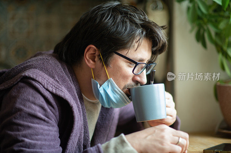 男子早上在厨房生病，戴着防护口罩，精疲力竭的病毒疾病