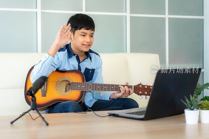 亚洲男孩弹奏吉他虚拟快乐时间会议在网上玩音乐与朋友在视频会议与笔记本电脑在网上会议在视频通话为社会距离。