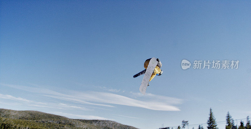 一个滑雪板在完整的冬季装备尝试“前侧360尾巴抓取”在跳跃在埃尔多拉滑雪度假村附近的博尔德，科罗拉多州在光明，阳光，冬天的一天