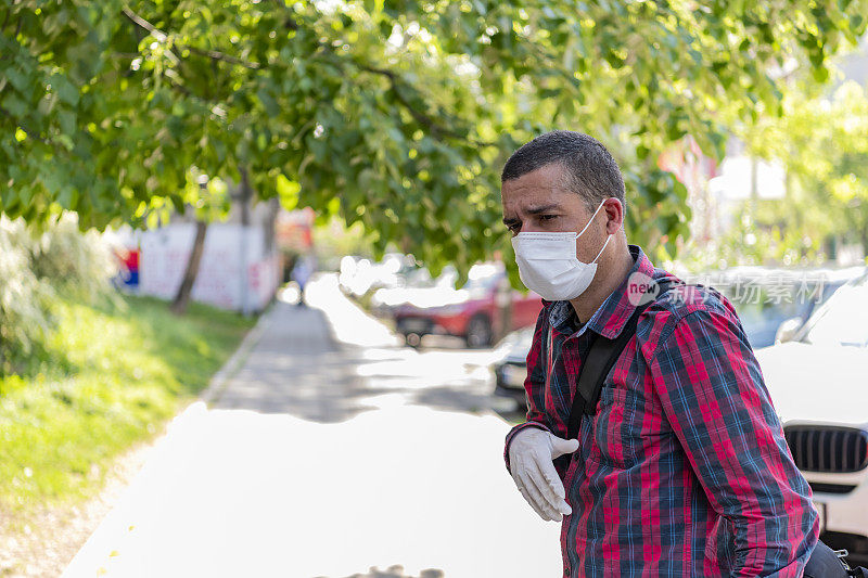 戴着面罩和防护手套的成年男子在街上咳嗽。