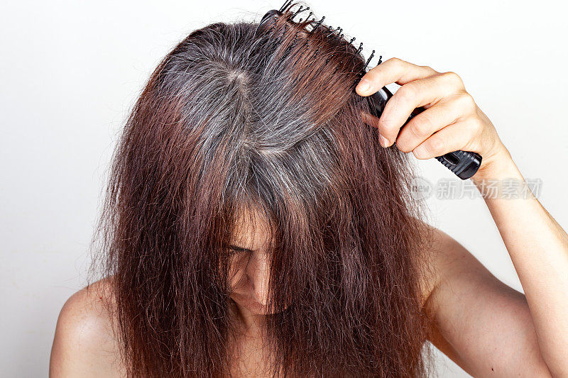 成年妇女用梳子梳起灰白的头发。