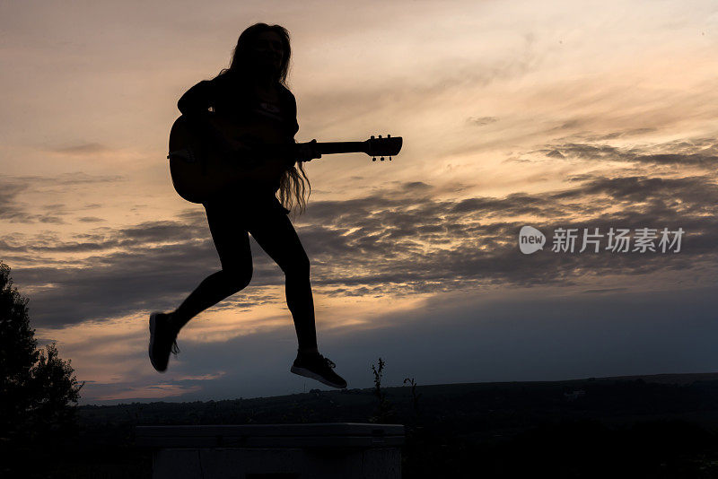 在落日的背景下，一个拿着吉他的女人的剪影