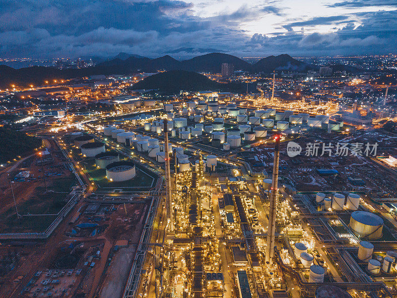 鸟瞰图在日落黄昏的大型化工厂，炼油厂，发电厂与原油储罐工作在日出附近的山区绿色环境概念