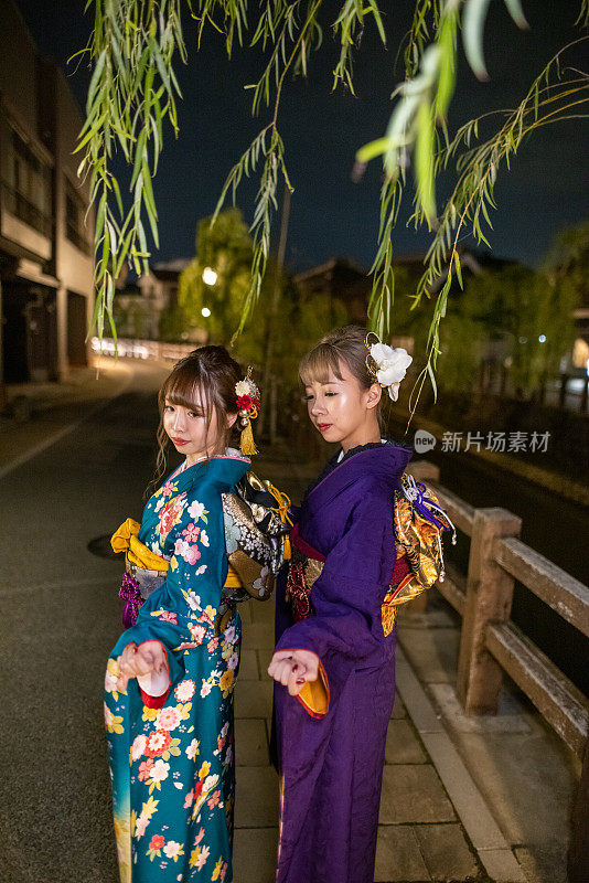 身着Furisode和服的年轻妇女在夜晚站在传统村庄的肖像